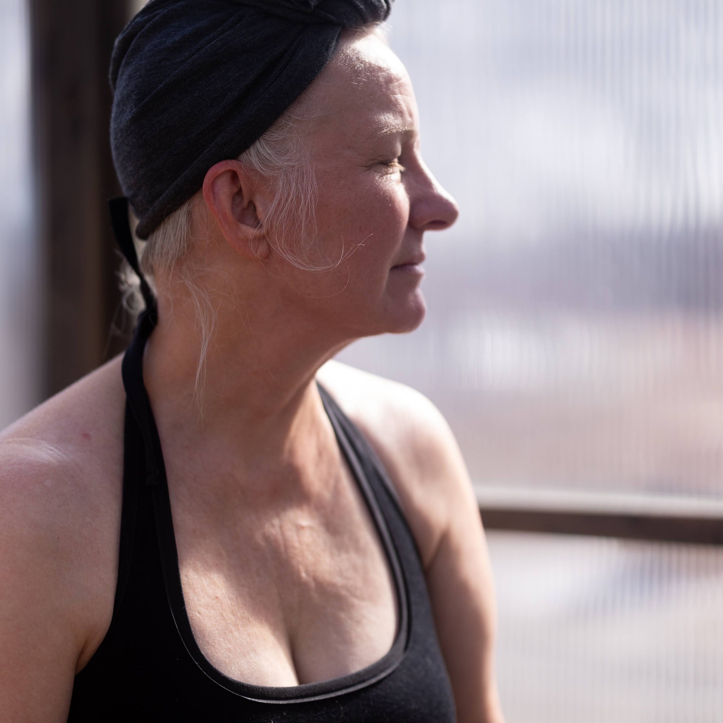 Woman wearing a black tank top and headscarf, standing indoors with a blurred background