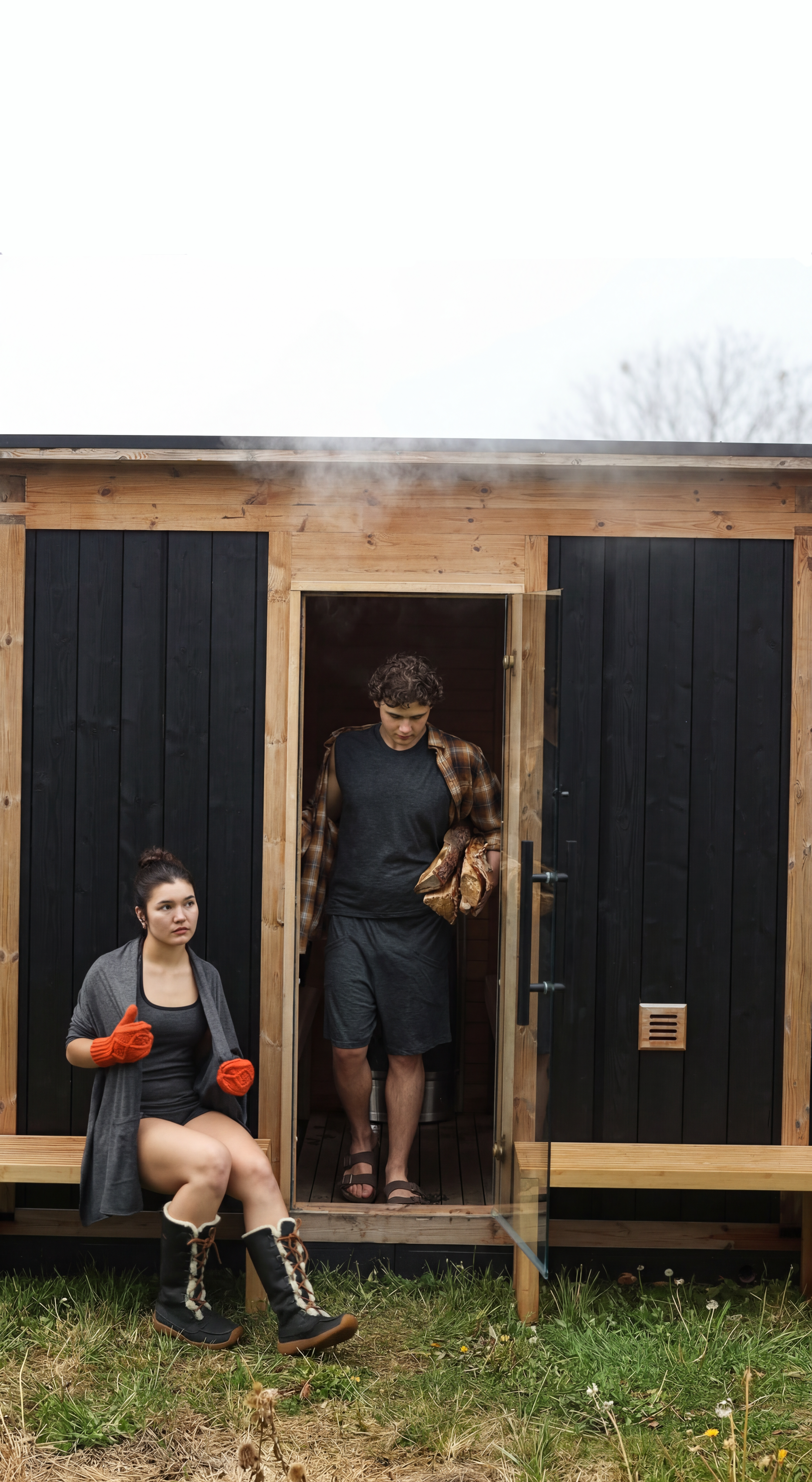 Two people standing outside a small wooden cabin with black doors.