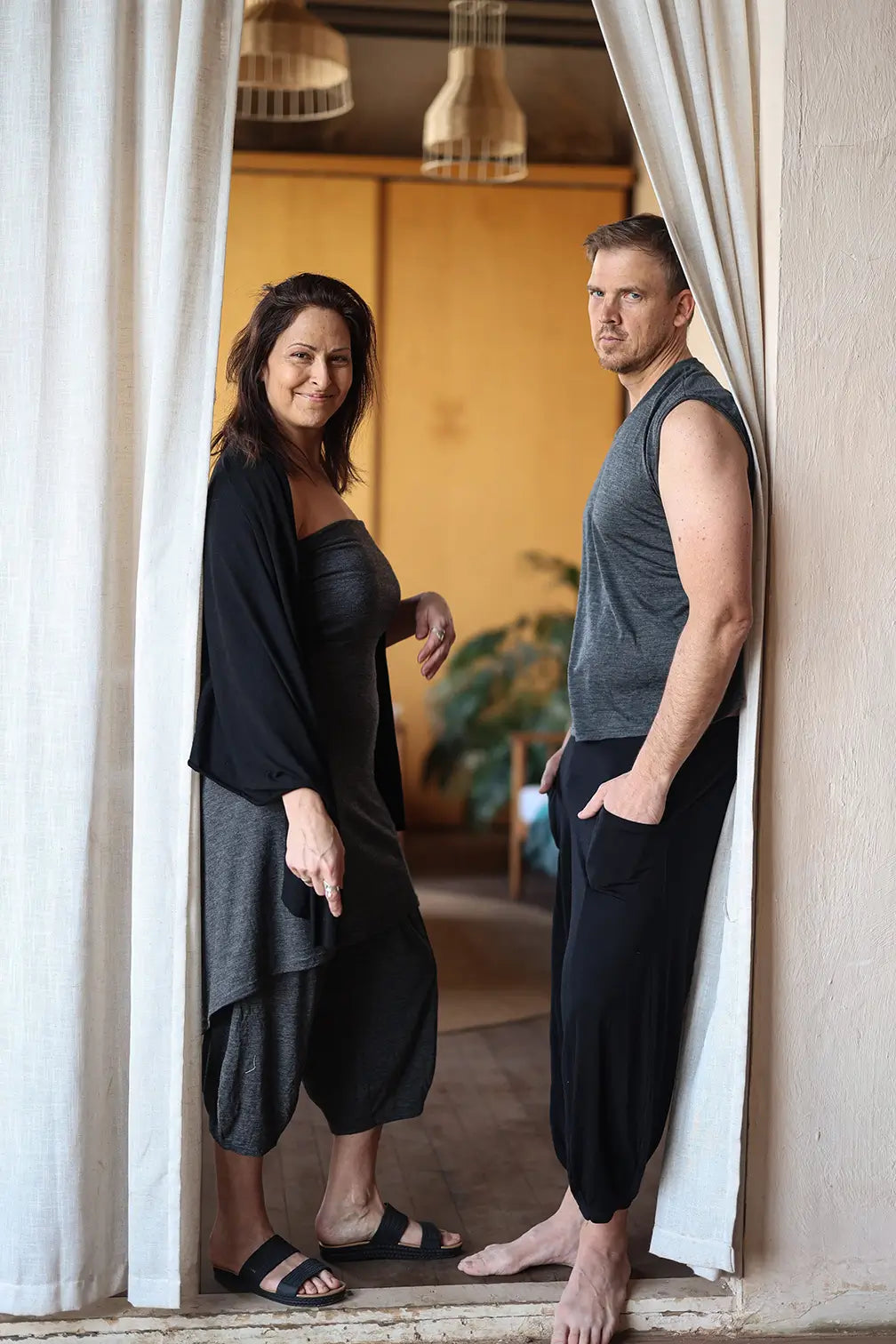 Two people standing in a doorway with white curtains, one person leaning against the wall.